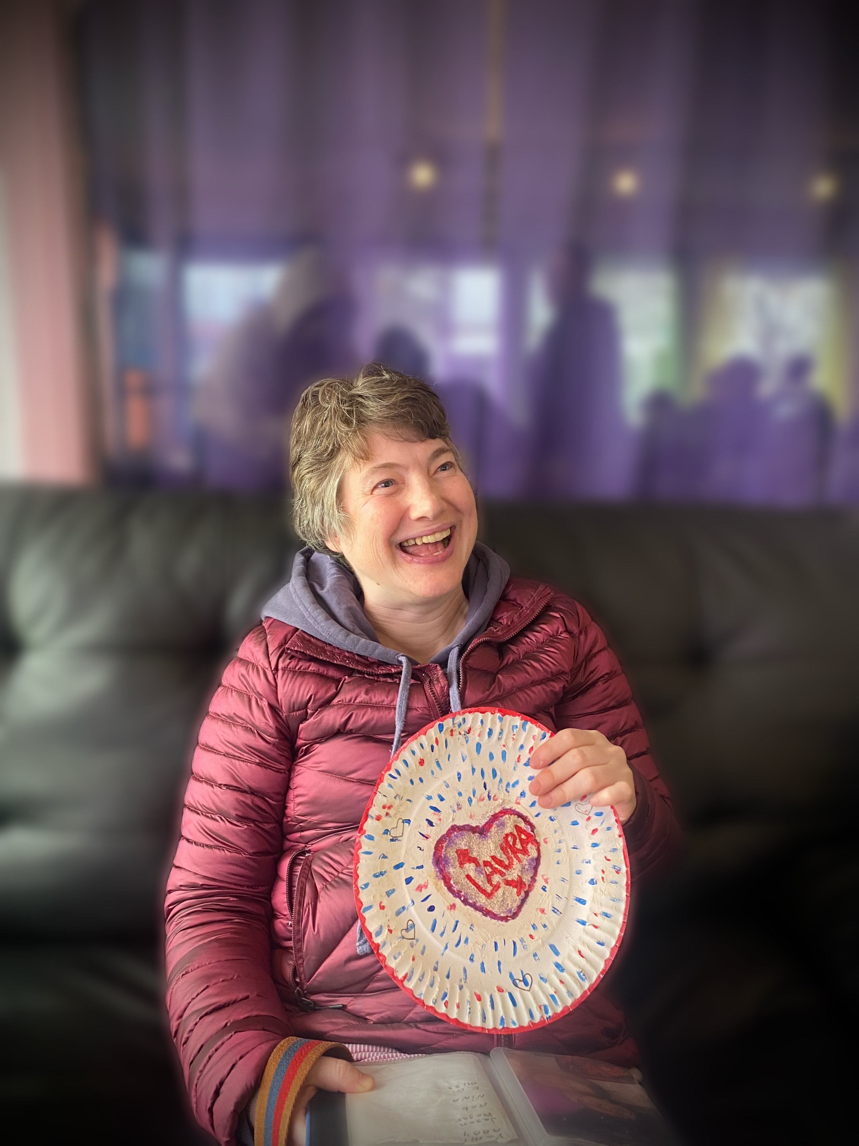 A client smiling and sitting on a sofa, holding a craft project.
